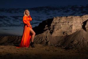 femme dans Orange robe avec svelte nu jambes posant près le le sable colline photo