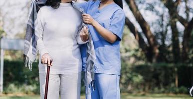 asiatique Jeune soignant infirmière soutien Sénior plus âgée Masculin en marchant en plein air. spécialiste fille médecin Aidez-moi et prendre se soucier de personnes âgées mature homme patient Faire physique thérapie dans Publique parc à allaitement maison. photo