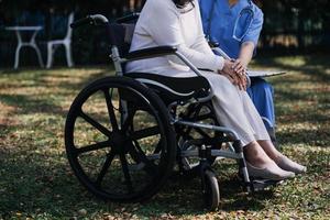 asiatique Jeune soignant infirmière soutien Sénior plus âgée Masculin en marchant en plein air. spécialiste fille médecin Aidez-moi et prendre se soucier de personnes âgées mature homme patient Faire physique thérapie dans Publique parc à allaitement maison. photo