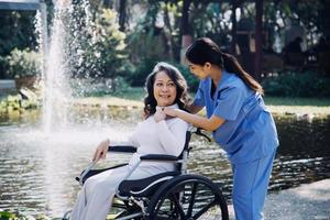 asiatique Jeune soignant infirmière soutien Sénior plus âgée Masculin en marchant en plein air. spécialiste fille médecin Aidez-moi et prendre se soucier de personnes âgées mature homme patient Faire physique thérapie dans Publique parc à allaitement maison. photo