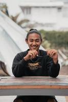 un asiatique homme avec le sien cheveux lié en haut et portant une noir chandail veste est séance relaxant à une café table lorsque réunion le sien copains photo