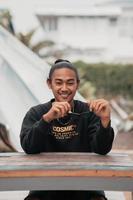 un asiatique homme avec le sien cheveux lié en haut et portant une noir chandail veste est séance relaxant à une café table lorsque réunion le sien copains photo