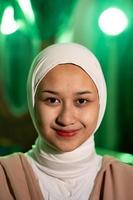 une musulman femme avec une blanc foulard et blanc vêtements souriant très jolie sans pour autant maquillage sur sa visage dans une vert pièce photo