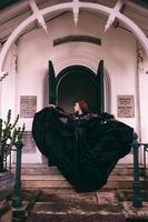 un élégant sorcière films sa tout noir robe dans le air dans de face de le cimetière portes après le Halloween Festival commence photo