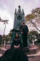 une couple de les amoureux séance et permanent dans de face de une funéraire monument dans tout noir vêtements et effrayant expressions sur Halloween photo