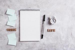 travail la vie équilibre concept. carnet de notes, stylo, alarme l'horloge et mots sur une gris Contexte. Haut voir. photo