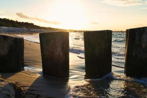 épis saillant dans le mer, à le coucher du soleil. plage avec des pierres dans le premier plan photo