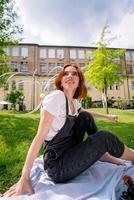 heureuse jeune femme assise sur une couverture sur la pelouse du parc photo