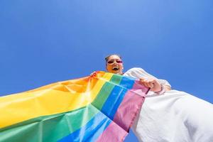 une jeune femme développe un drapeau arc-en-ciel contre le ciel photo