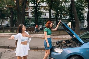 deux femmes avec une route de voiture cassée cherchent de l'aide. photo