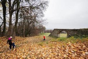 mère avec des gamins en marchant dans l'automne feuilles près vieux pierre cambre. photo
