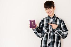 Jeune adolescent garçon en portant Roumanie passeport à la recherche positif et content permanent et souriant avec une sur de soi sourire contre blanc Contexte. photo