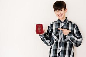 Jeune adolescent garçon en portant Serbie passeport à la recherche positif et content permanent et souriant avec une sur de soi sourire contre blanc Contexte. photo