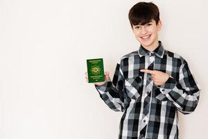 Jeune adolescent garçon en portant turkménistan passeport à la recherche positif et content permanent et souriant avec une sur de soi sourire contre blanc Contexte. photo