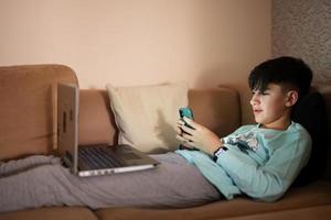 Jeune adolescent garçon envoyer des SMS téléphone dans de face de une portable sur une lit à soir. photo