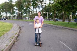 mignonne garçon dans une blanc T-shirt monte avec le sien papa sur une scooter photo