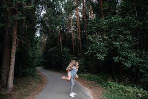 dans une vert forêt, une fille sauté sur une gars retour et elles ou ils rire photo