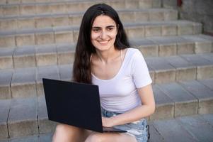 le fille est séance sur le escaliers, portable sur sa genoux, à la recherche une façon photo