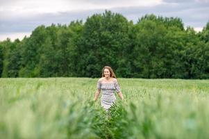 une mignonne fille avec longue cheveux dans une robe court par une blé champ photo