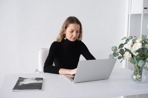 le fille travaux dans une blanc Bureau avec une portable et fleurs sur le table photo