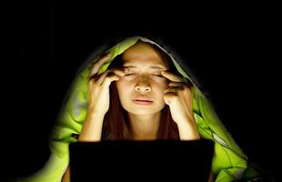 asiatique femmes souffrir de fatigue des yeux de à la recherche à des ordinateurs dans faible lumière. regarder films en ligne photo