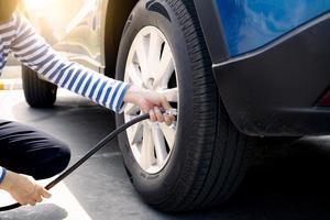 la femme gonfle le pneu. femme vérifiant la pression des pneus et pompant de l'air dans le pneu de la roue de la voiture. service d'entretien de voiture pour la sécurité avant le voyage. point de gonflage des pneus. remplissage d'air dans le pneu de la voiture photo