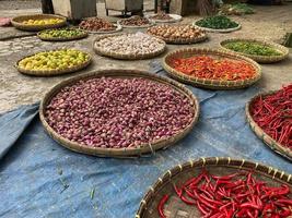 divers des légumes tomates, Chili, rouge oignon, maïs, carotte, chaux, Ail étant vendu à asiatique traditionnel marché. coloré des légumes sur rond bambou plateau à traditionnel marché sol photo