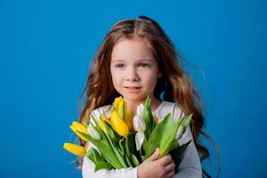 portrait de une charmant souriant peu fille avec une bouquet de tulipes dans sa mains. mode de vie. Frais fleurs. international aux femmes journée. espace pour texte. haute qualité photo