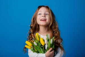 portrait de une charmant souriant peu fille avec une bouquet de tulipes dans sa mains. mode de vie. Frais fleurs. international aux femmes journée. espace pour texte. haute qualité photo