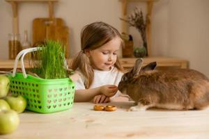 mignonne peu fille dans le en bois cuisine de le maison alimente le lapin Frais herbe photo