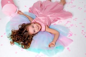 magnifique peu fille dans une élégant rose robe mensonges sur le sol jonché avec confettis. Haut voir. mode et style. enfant fête le sien anniversaire. photo dans le studio. espace pour texte. haute qualité photo