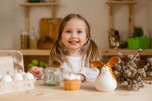 mignonne peu fille dans une coton robe à Accueil dans une en bois cuisine prépare un Pâques gâteau photo