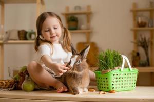 mignonne peu fille dans le en bois cuisine de le maison alimente le lapin Frais herbe photo