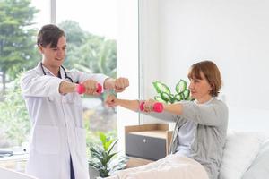 femelle patient exercice avec haltères dans le hôpital. physiothérapeute assistant Sénior femme à ascenseur haltères. le médecin est examiner le patient dans le hôpital photo