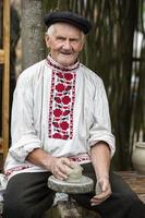 Biélorussie, le village de lyaskovichi. août 20, 2022. une vacances de ethnique des cultures. un vieux slave homme dans une biélorusse lin brodé chemise sculpte articles de argile. ethnique nationale artisanat. photo