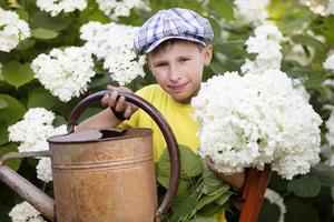 l'enfant travaille dans le jardin. garçon avec un arrosoir vintage et un bouquet de fleurs. photo