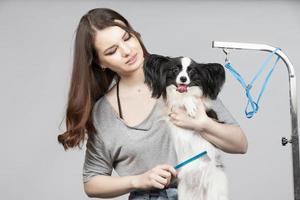 Jeune professionnel toiletteur avec animaux domestiques. elle est posant avec un instrument. papillon chien et fille coiffeur. photo