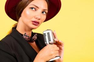 fille dans une noir costume sur une Jaune Contexte chante dans une rétro microphone, portrait, la musique photo