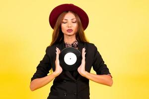 fille dans une noir costume sur une Jaune Contexte avec une record dans sa mains, musique, le fille spectacles émotions photo