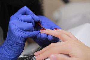 maître en gants de protection lors d'une manucure au salon de beauté. le maître manucure vernit le gel de marsala sur les ongles d'une cliente. le concept de beauté et de santé. photo