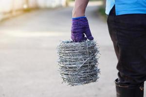 la main du travailleur en gros plan tient des rouleaux de fil de fer barbelé. concept, outil de construction. le fil de fer barbelé est utilisé pour faire des clôtures, sécuriser la propriété, faire une frontière pour montrer le territoire de la zone. photo