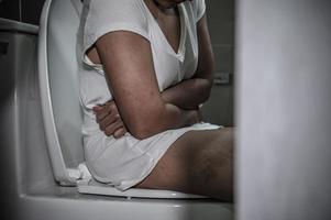 avoir problèmes avec excrétion concept, un asiatique femme est assis sur le toilette bol, constipation et une longue temps dans le toilettes. photo