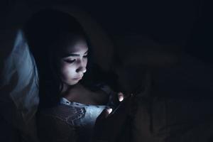 femme asiatique jouant au jeu sur smartphone dans le lit la nuit, thaïlande, toxicomane médias sociaux photo