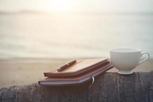 cahiers, livres, stylo et une tasse de café sur la plage photo