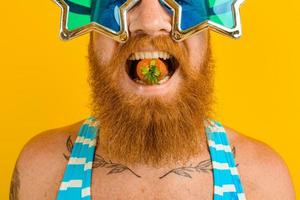 homme avec barbe et des lunettes de soleil mange une fraise photo