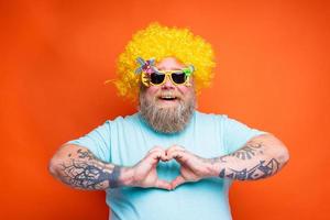 graisse content homme avec barbe, tatouages et des lunettes de soleil fait du cœur forme avec mains photo