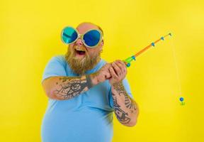 graisse homme avec barbe et des lunettes de soleil avoir amusement avec le pêche barre photo