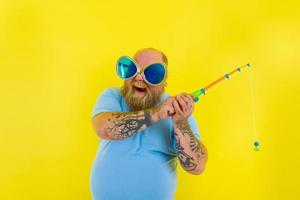 graisse homme avec barbe et des lunettes de soleil avoir amusement avec le pêche barre photo
