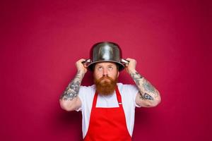 inquiet chef avec barbe et rouge tablier pièces avec pot photo