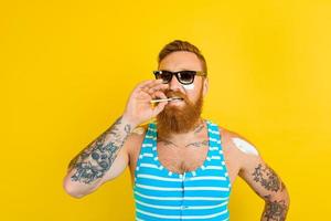 homme avec barbe, tatouage et maillot de bain fume une cigarette photo